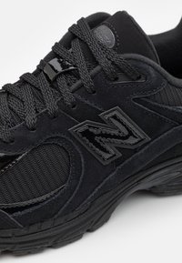 Černá sportovní bota s kombinací semišového a síťovaného materiálu, silnou texturovanou podrážkou a výrazným černým logem na boku.