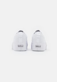 Vita sneakers med perforerade ovandelar, platta gummisulor och stickade detaljer. Har en märkesetikett och en dragflik baktill för enkel påtagning.