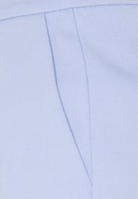 Ljust blått tyg med en strukturerad väv och synlig sömnad. Inkluderar en enkel veckdetalj längs kanten som förbättrar strukturen.