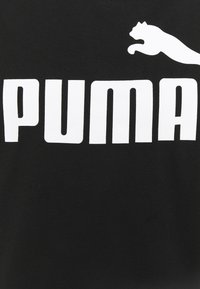 T-shirt preta em algodão com o ousado texto branco "PUMA" e um logo de gato saltando acima do nome da marca. Textura suave e design clássico.