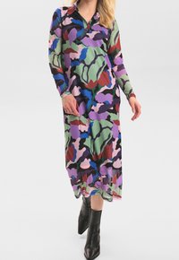 Långärmad klänning i ett flerfärgat kamouflage-mönster med gröna, lila, röda och blå nyanser, med krage och knapppdetaljer.