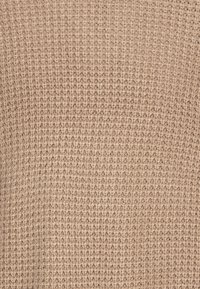 Beige Strickstoff mit einem strukturierten, offenen Webmuster, das ein weiches, natürliches Material zeigt, das sich gleichmäßig über die gesamte Oberfläche erstreckt.