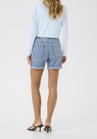 Haut bleu clair à manches longues associé à un short en denim taille haute aux revers roulés. Le short présente un design classique à cinq poches.