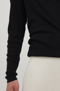 Schwarzer Strickpullover mit eng anliegenden langen Ärmeln und einem gerippten Textur, kombiniert mit einem hellbeigen, gerippten Unterteil.