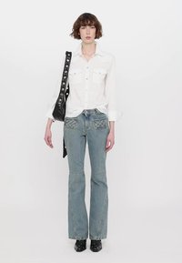 Vit långärmad skjorta med två bröstfickor, ihop med ljusblå utsvängda jeans med dekorativ sömnad och svarta ankelstövlar.