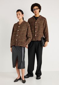 Dva modely nosia zladené bordové a zelené textúrované pletené kardigany s gombíkmi, skombinované s čiernou koženou sukňou a upravenými nohavicami.