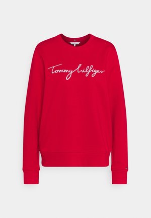 Red sweatshirt with long sleeves, round neckline, and white "Tommy Hilfiger" logo in cursive across the chest. Cotton material with ribbed cuffs.