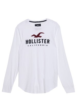 Chemise blanche en coton à manches longues avec col rond, comportant un logo de mouette bordeaux et le texte « HOLLISTER CALIFORNIA » sur le devant.