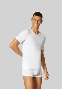 Witte T-shirt met korte mouwen en V-hals, slim fit ontwerp, gemaakt van zachte stof, gecombineerd met witte boxers, model staat tegen een grijze achtergrond.