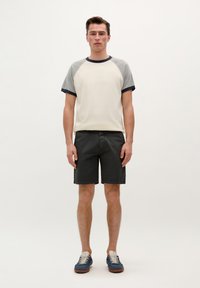 Camiseta raglán de mangas cortas en color crema con mangas grises, combinada con pantalones cortos negros y zapatillas azules con cordones beige y suelas de goma.