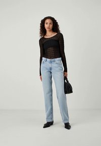 Svart langermet mesh-top med et teksturert mønster, kombinert med lyseblå, rette jeans. Modellen holder en svart håndveske.