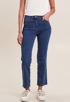 Lichtblauwe denim jeans met een recht model, een middelhoog taille, voorzakken en subtiele stikseldetails. Gecombineerd met witte sneakers.