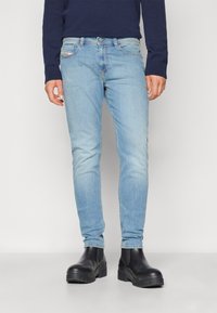 Világoskék farmernadrág, slim fit szabással, öt zsebbel és enyhe kopással. Fekete bokacsizmával párosítva, kontrasztos megjelenésért.