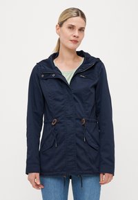 Veste bleu marine avec capuche, taille à cordon de serrage, poches avant doubles et poche poitrine zippée. Tissu doux avec des détails de couture subtils.