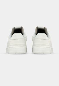 Bílé kožené tenisky s texturovaným povrchem, plochou gumovou podrážkou a polstrovaným límcem na patě. Vyznačují se minimalistickým designem bez viditelného loga.