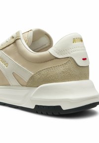 Baskets en daim beige et blanc avec semelle blanche épaisse, semelle extérieure noire, logo doré « HUGO » sur le côté, et languette de talon blanche avec détails de couture dorée et rouge.