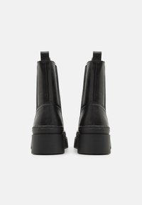 Schwarze Leder-Stiefeletten mit einer klobigen Plateausohle, verticalen Nähten, Zuglaschen und einer glatten Textur.