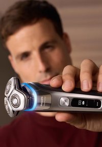 Philips 9000 Prestige elektrisch scheerapparaat, metallic grijs met drie ronde koppen, blauw licht, digitaal display en ergonomische grip.