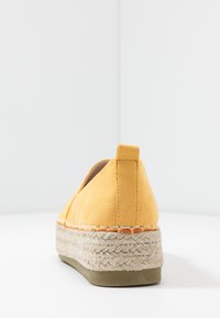 Gul ruskindsespadrille med en vævet jutesål og beige bund, der har lukket bag og minimale syninger.