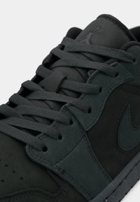 Σκούρες γκρι αθλητικά παπούτσια φτιαγμένα από σουέντ και συνθετικά υλικά, με επίπεδα κορδόνια, υφή και ανάγλυφο λογότυπο στη γλώσσα.