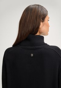 Maglione nero a collo alto lavorato a maglia con texture a coste, con un'etichetta logo sul retro. Design semplice e dal taglio rilassato.