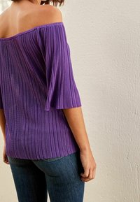 Top viola, scollato sulle spalle, con una texture a righe verticali. Maniche svasate e una vestibilità comoda, abbinato a jeans in denim scuro.
