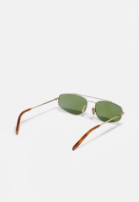 Ochelari de soare cu rame din metal aurit și lentile verzi, având un design cu pod dublu și vârfuri de brad țestoasă. Ușori și eleganți.