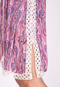 Klänning med rosa och lila spiraler, prydd med vit spetskant och en sidoslits. Tillverkad av lätt material, har den ett flödande och texturerat utseende.