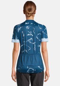 Jersey de ciclismo de manga corta en teal con patrones de animales blancos, que presenta una textura de malla transpirable y una parte posterior fruncida para mayor flexibilidad.