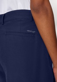 Temno modri hlače z elegantnim dizajnom, izdelane iz gladkega materiala. Imajo zadnji žep in subtilno vezenje logotipa "VENTUS7".