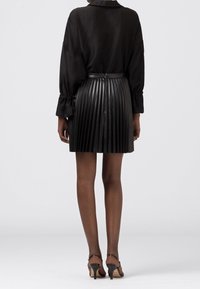 Blouse en soie noire avec une mini-jupe plissée en faux cuir noir. Présente une taille ajustée et une texture brillante. Des talons noirs à lanières complètent le look.