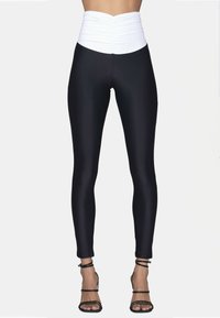 Leggings neri con una vita alta e arricciata di colore bianco. Tessuto liscio con una vestibilità skinny. Indossati con sandali neri con cinturini, che mettono in risalto i dettagli della caviglia.