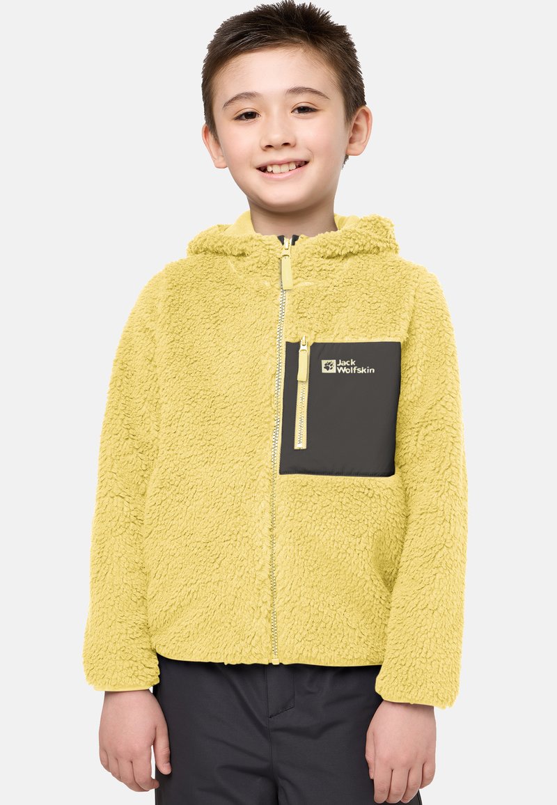 Keltainen fleece-takki hupulla, jossa on musta vetoketjullinen rintatasku ja kevyet vetoketjuakcentit. Pehmeä rakenne, rento muotoilu.