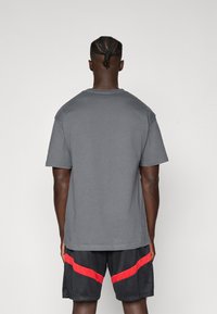 Grå bomulds T-shirt med korte ærmer, rund hals og lige skæring. Bæres med sorte træningsshorts med røde vandrette striber.