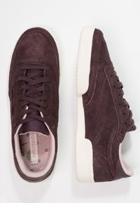 Mörklila mockaskor med rund tå, snörning framtill och något texturerad vit gummisula. Inredning med blommönster.