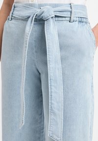 Lichtblauwe denim broeken met een gestrikt taille-detail. Heeft een relaxte pasvorm, zijzakken en een zachte textuur. Klassiek vijf-pocket ontwerp.