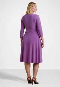 Violetti mekko, jossa on kolmasosa hihat, muotoiltu vartalo ja levenevä hame. Sujuva rakenne ja vyöyksitys vyötäröllä. Yhdistetty ruskeisiin korkokenkiin.