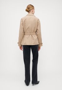 Cappotto beige con cintura, colletto e maniche lunghe, abbinato a pantaloni neri a gamba larga. Texture liscia, design semplice, hardware ridotto al minimo.