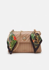 Bež prešivana torbica s remenom od zlatnog lanca, ukrašena kopčom u obliku tigrove glave i ukrasnim maramama s tropskim uzorcima u zelenoj i narančastoj boji.
