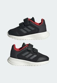Černé sportovní boty s červenými akcenty, vyrobené z pletiva a syntetických materiálů, s uzávěrem na suchý zip a třemi šedými pruhy po stranách.