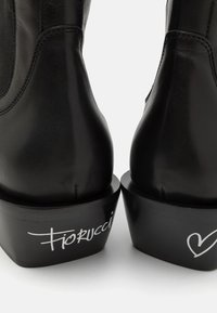 Botines de cuero negro con paneles laterales elásticos, que cuentan con una suela de plataforma y el logo blanco "Fiorucci" en el talón. Textura suave, forma redondeada.