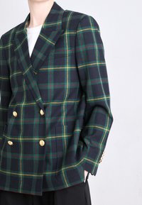 Blazer croisé en écossais bleu marine, avec des lignes vertes et jaunes, des boutons dorés, et une coupe ajustée avec poches. Tissu texturé.