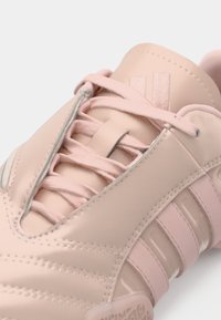 Αθλητικό παπούτσι σε ανοιχτό ροζ χρώμα, κατασκευασμένο από λείο συνθετικό υλικό, με κορδόνια και τρεις οριζόντιες ρίγες στο πλάι.