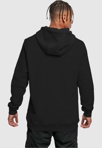 Hoodie noir avec une poche kangourou à l'avant et une capuche à cordon. Le tissu semble doux et légèrement texturé. Poignets et ourlet côtelés.