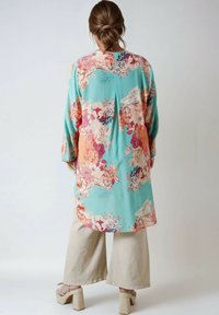 Kimono floral en tissu turquoise, avec des motifs floraux roses et corail, coupe ample et manches longues, avec un détail de pli à l'arrière.