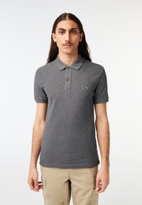 Camisa polo gris hecha de tela texturizada, con un cuello, tres botones y un pequeño logo verde en el lado izquierdo del pecho. Mangas cortas.