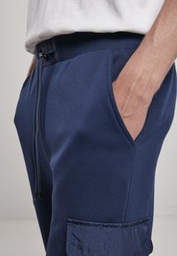 Marineblauwe joggingsbroek met een verstelbare tailleband, zijzakken en een geprofileerde patch pocket. Gemaakt van zachte, gladde stof met geribbelde accenten.