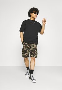 Svart kortärmad T-shirt, kamouflagemönstrade cargoshorts med fickor, svarta högsneakers och solglasögon; avslappnad outfit med en ledig passform.