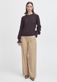 Purple textured knit sweater with long sleeves, paired with wide beige trousers. Brown heeled shoes complete the outfit.