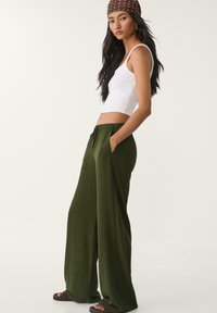 Biała bluzka typu crop top połączona z szerokimi, oliwkowymi spodniami. Spodnie mają elastyczny pasek w talii oraz kieszenie, wykonane są z miękkiego, teksturowanego materiału.